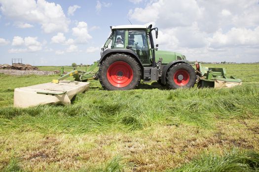 tractor and mower in green meadow in the netherlands on sunny day