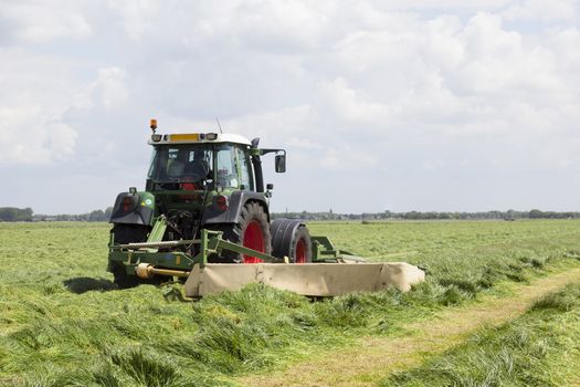 tractor and mower in green meadow in the netherlands on sunny day