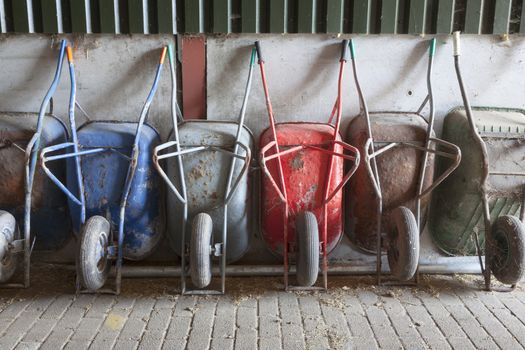 six old and rusty wheelbarrows rest against wall of farm barn