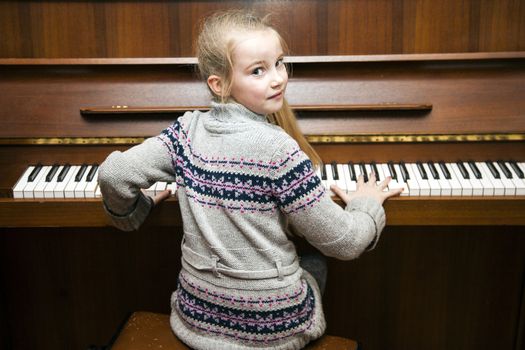 young girl plays brown  upright piano and smiles