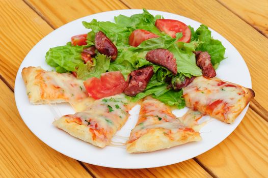 Pizza slices with melted cheese and fresh vegetables salad