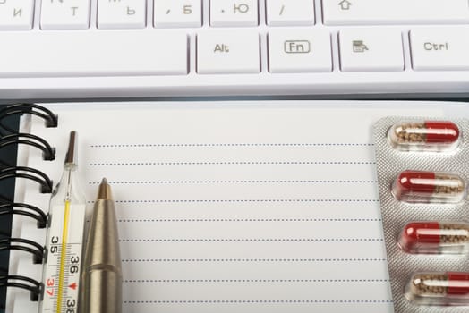 Notebook and keyboard with thermometer, drugs, close up view