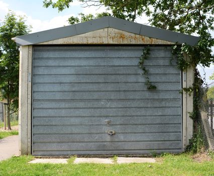 Free-standing garage with a locked, unpainted metal door, overgrown with ivy