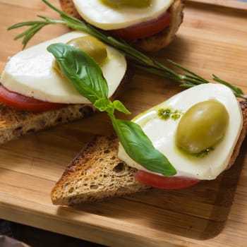 Bruschetta with tomato, mozarella and olive on wooden table 