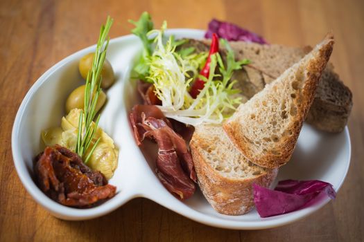 Antipasto. Dried tomatoes, olives, prosciutto and bread in a white plate. Shallow dof