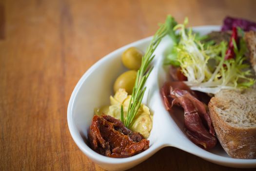 Antipasto. Dried tomatoes, olives, prosciutto and bread in a white plate. Shallow dof