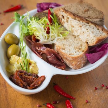 Antipasto. Dried tomatoes, olives, prosciutto and bread in a white plate. Shallow dof