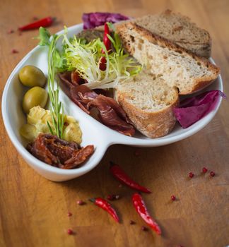 Antipasto. Dried tomatoes, olives, prosciutto and bread in a white plate. Shallow dof