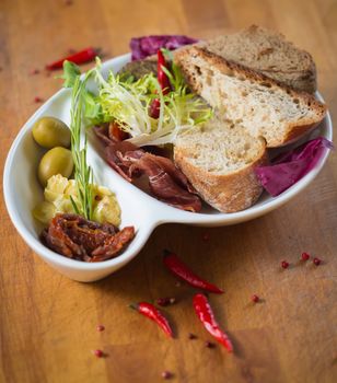 Antipasto. Dried tomatoes, olives, prosciutto and bread in a white plate. Shallow dof