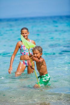 Cute boy and his sister playing with scoop-net and swimming in the transparent sea