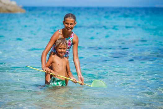 Cute boy and his sister playing with scoop-net and swimming in the transparent sea