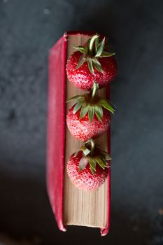 Strawberries and  red cook book on a dark table