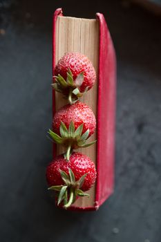 Strawberries and  red cook book on a dark table