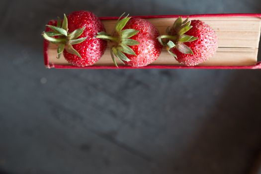 Strawberries and  red cook book on a dark table