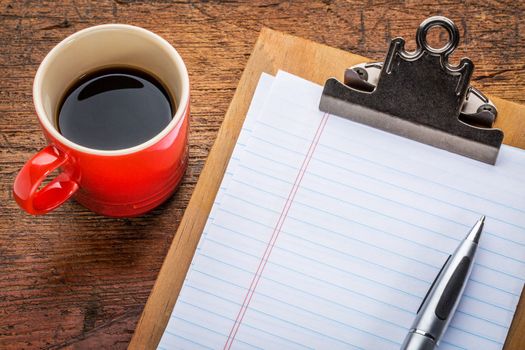 blank paper on clipboard and coffee against grunge wood desk - office concept