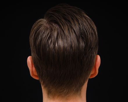 Rear view of hairstyle on male person with brown hair at closeup isolated towards black background