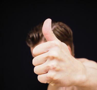Caucasian male showing thumbs up covering face isolated on black