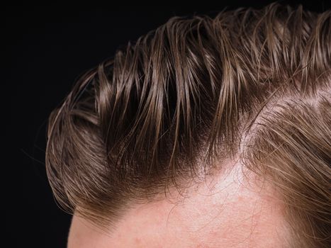 Hairstyle on male person with brown hair at closeup isolated towards black background