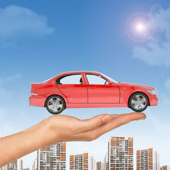 Red car above businesswomans hand with cityscape on blue sky background 