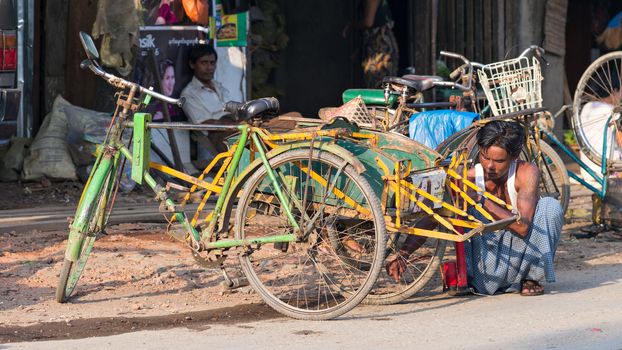 Sittwe, Rakhine State, Myanmar - October 15, 2014: Man repairing a bicycle taxi at the roadside in Sittwe, the capital of the Rakhin State in Myanmar.