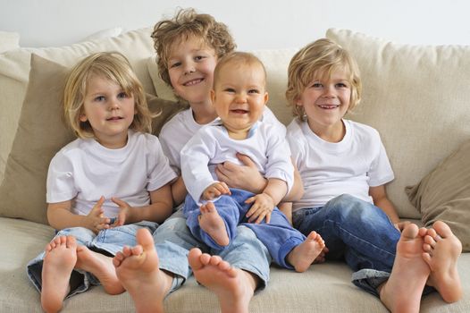 Four brothers, young boys, sitting on a sofa. The eldest is holding a baby in his lap.  They're looking to the right of camera