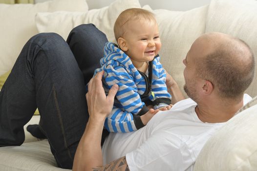 Father lying on a couch holds his baby son in his lap