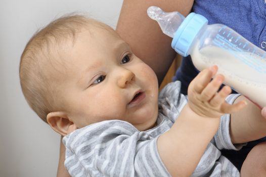 Seven month old baby grasping milk bottle in his mother's arms. 