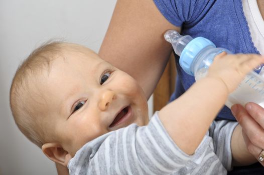 Seven month old baby boy bottle feeding in his mother's arms. 