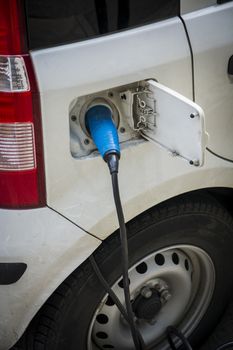 Charging an electric car at a roadside urban charging station showing a close up of the attached connector and cable in a green energy concept