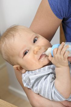 Seven month old baby boy bottle feeding in his mother's arms. 