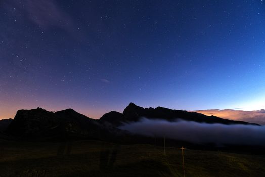 evening at the Rolle pass with fog on the mountains and blue sky with stars background, Trentino - Italy