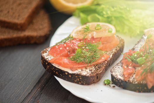 Homemade sandwich with salmon and rye bread , butter lemon, and lettuce for breakfast