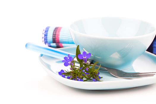 tableware with blue lobelia flowers and cutlery, on a white background.