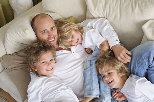 Children climbing over their father on the sofa