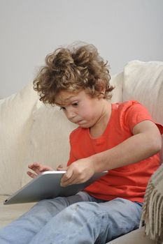 An 8-9 year old boy plays games on a touch screen tablet. He's sitting on a sofa