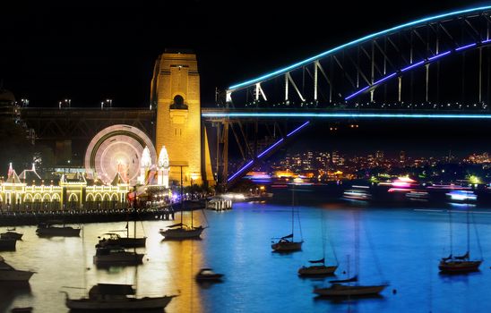 MILSONS POINT, AUSTRALIA - JUNE 6, 2015;  Luna Park and Sydney Harbour Bridge with boats and ferries in motion by night.