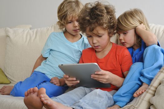 An 8-9 year old is playing a game on a touch screen tablet. His younger brothers are watching every move intently