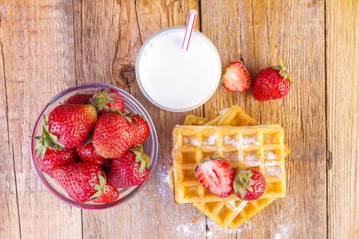 homemade waffles with strawberries and glass with milk on wooden background