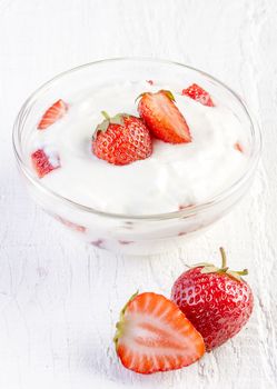 fresh organic yogurt with strawberries on white wooden background