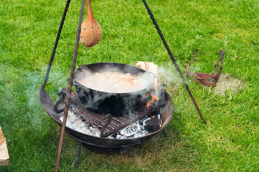 Cooking traditional country soup over burning campfire in cast iron pot                               