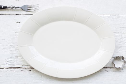 Top view of empty oval ceramic plate, fork and flower shape cookie cutter putting on white wooden table. retro, vintage and country style image