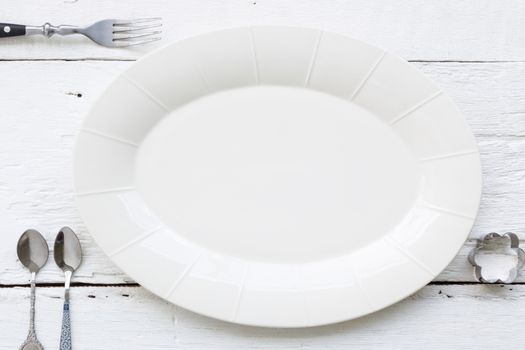 Top view of empty oval ceramic dish, fork, teaspoons and flower shape cookie cutter putting on white wooden table. retro, vintage and country style image