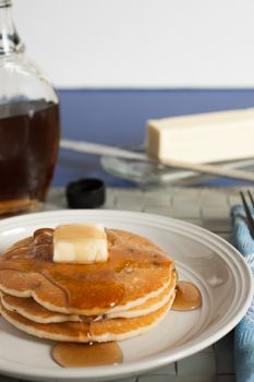 Fresh pancakes on a white plate with maple syrup and butter.