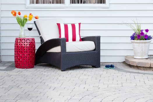 Single armchair with a red ceramic pedestal table and vase of spring tulips with a matching striped red and white cushion on a brick paved outdoor patio for a relaxing break