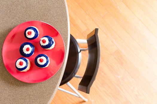 Patriotic 4th July Independence Day cupcakes with red, white and blue icing served on a red plate on a table, overhead view with copyspace on a wooden parquet floor