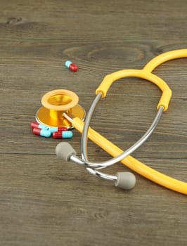 Yellow stethoscope and medicine capsules placed on a wooden floor.                               