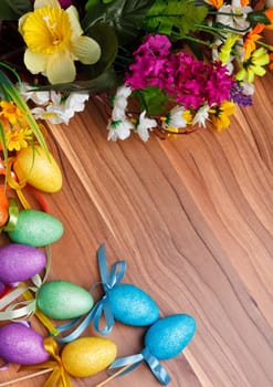 Easter flower arrangement and colorful eggs on a wooden surface with space for text