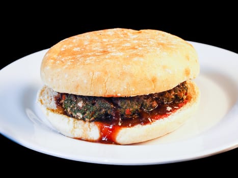 Closeup of juicy hamburger between buns with delicious red sauce on white plate towards black