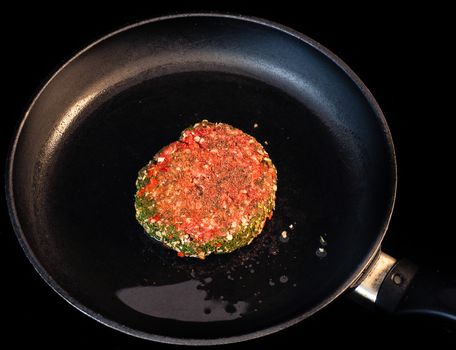 Raw red seasoned hamburger in fry pan isolated on black