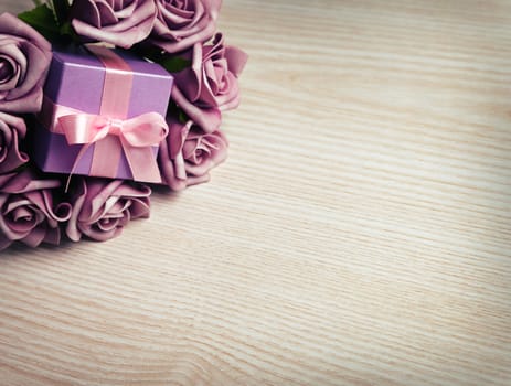 purple roses and gift box with pink ribbon on wooden surface with space for text
